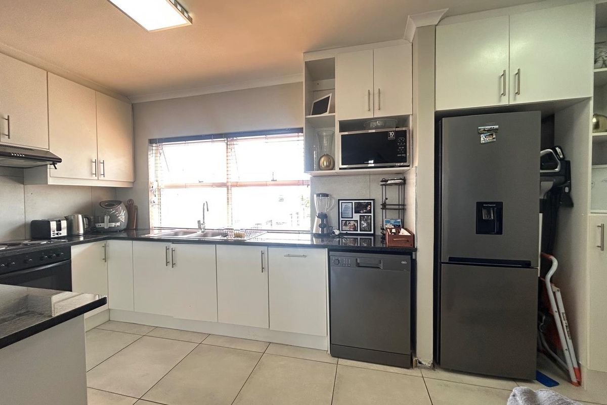 A functional kitchen featuring white cabinetry, dark granite countertops, a built-in oven, extractor fan, and tiled flooring with ample natural light.