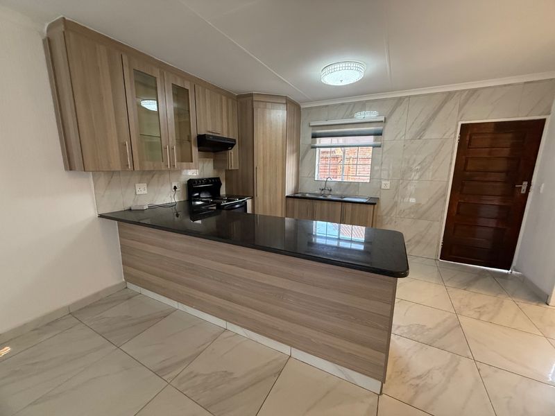 Modern kitchen featuring light wood cabinetry, dark granite countertops, tiled walls, and flooring, offering a clean and functional workspace.