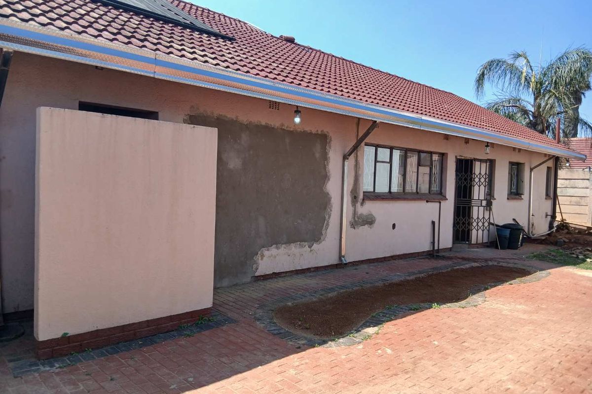 Rear exterior view of the house featuring a tiled roof, brick paved patio area, and unfinished plasterwork on the exterior wall.