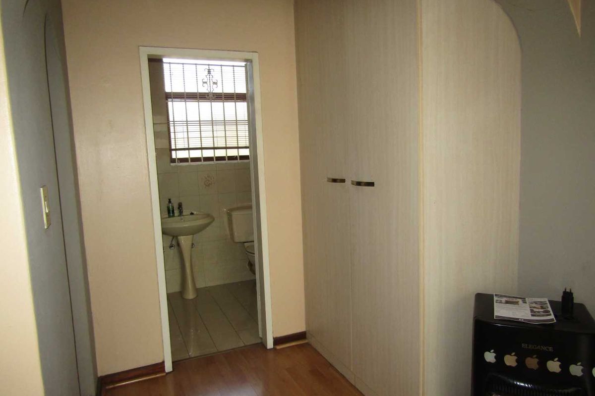A bedroom area featuring built-in cupboards and direct access to an en-suite bathroom with a pedestal basin and toilet.