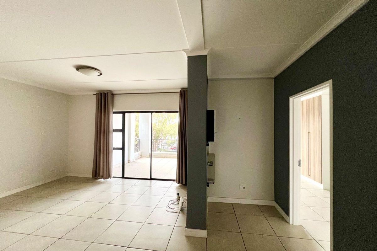 Spacious, light-filled living area featuring neutral tiled flooring, a modern accent wall, and direct access to an outdoor balcony through sliding glass doors.