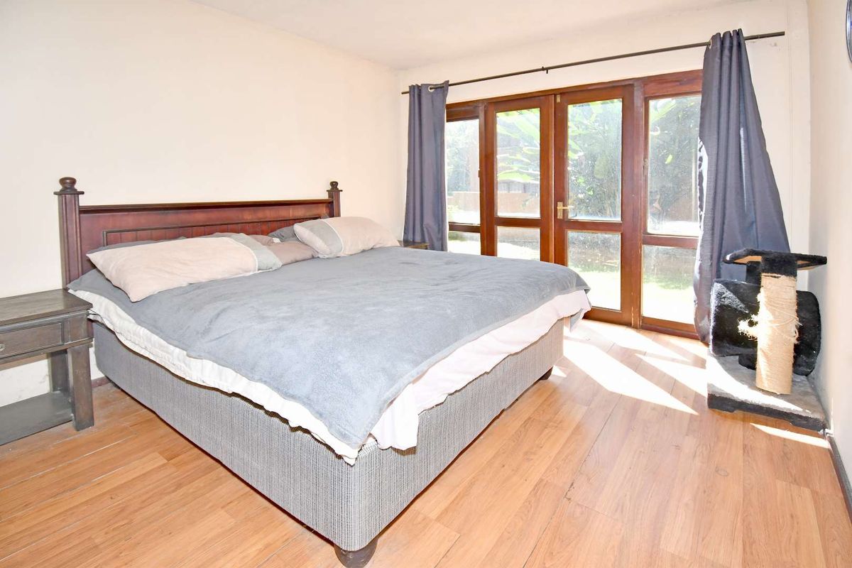 A bedroom featuring laminate flooring and large wooden-framed glass doors providing direct access to the outdoor area.