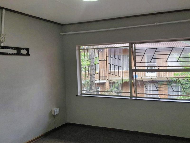 An empty bedroom featuring a large window with security bars, wall-mounted television bracket, and neutral wall finishes.