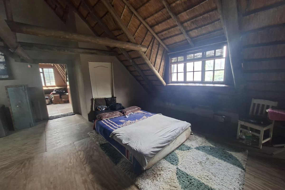 Spacious attic-style bedroom featuring exposed timber beams, a traditional thatched roof, and natural light through a multi-pane window.