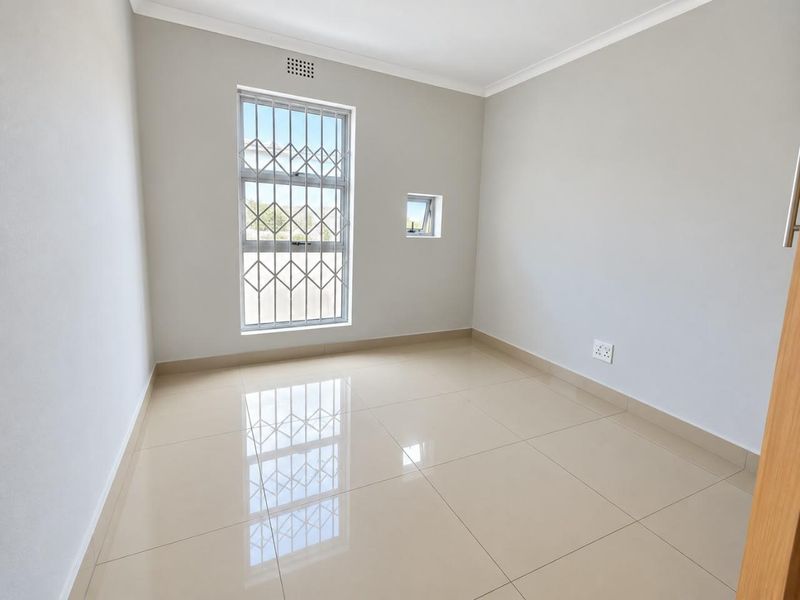 A bright, empty bedroom featuring neutral tiled flooring, clean walls, and security bars on the windows, providing a blank canvas for personalization.