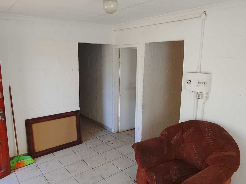 A basic living area featuring tiled flooring and exposed masonry walls, requiring cosmetic updates and electrical finishing to improve the space.
