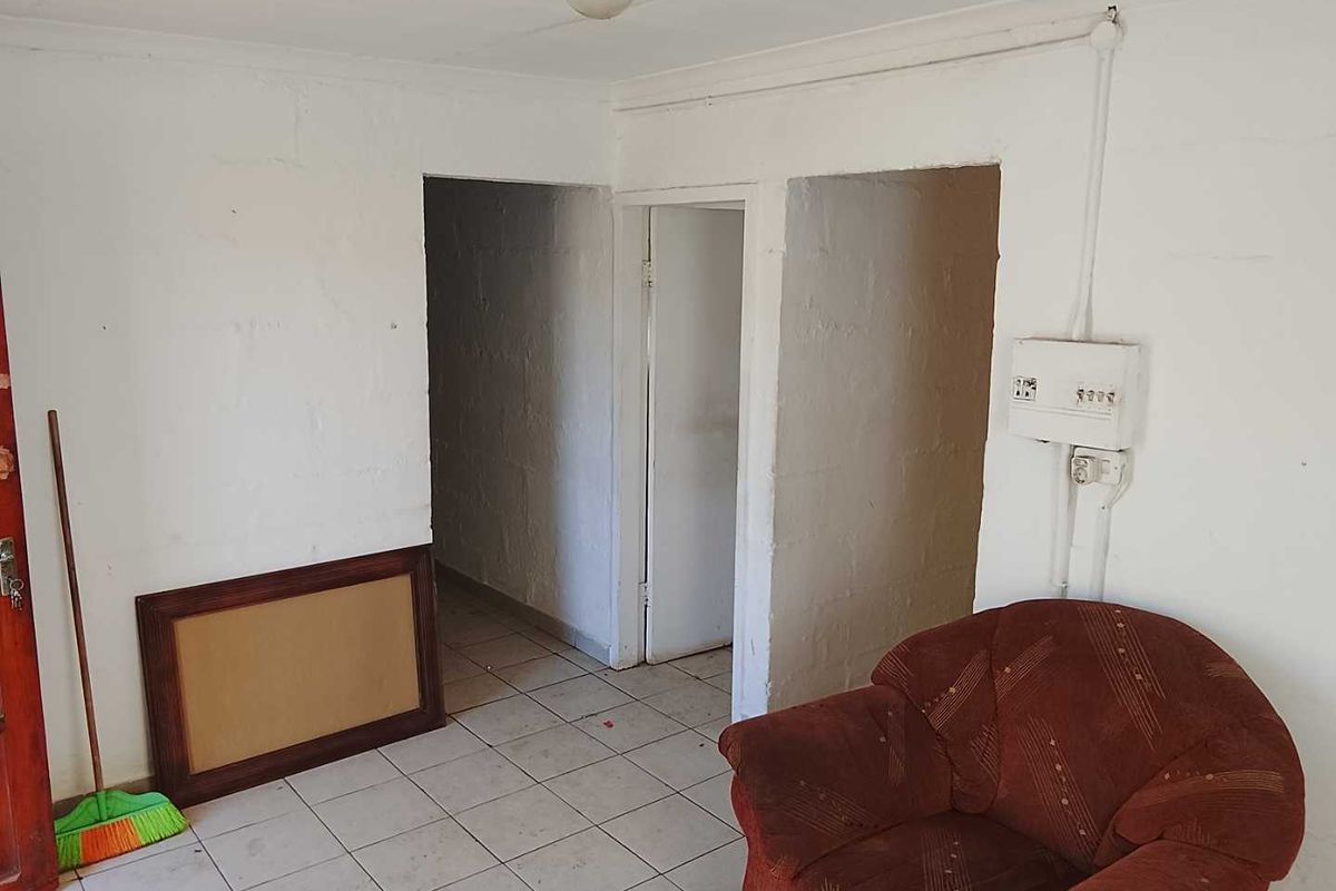 A basic living area featuring tiled flooring and exposed masonry walls, requiring cosmetic updates and electrical finishing to improve the space.