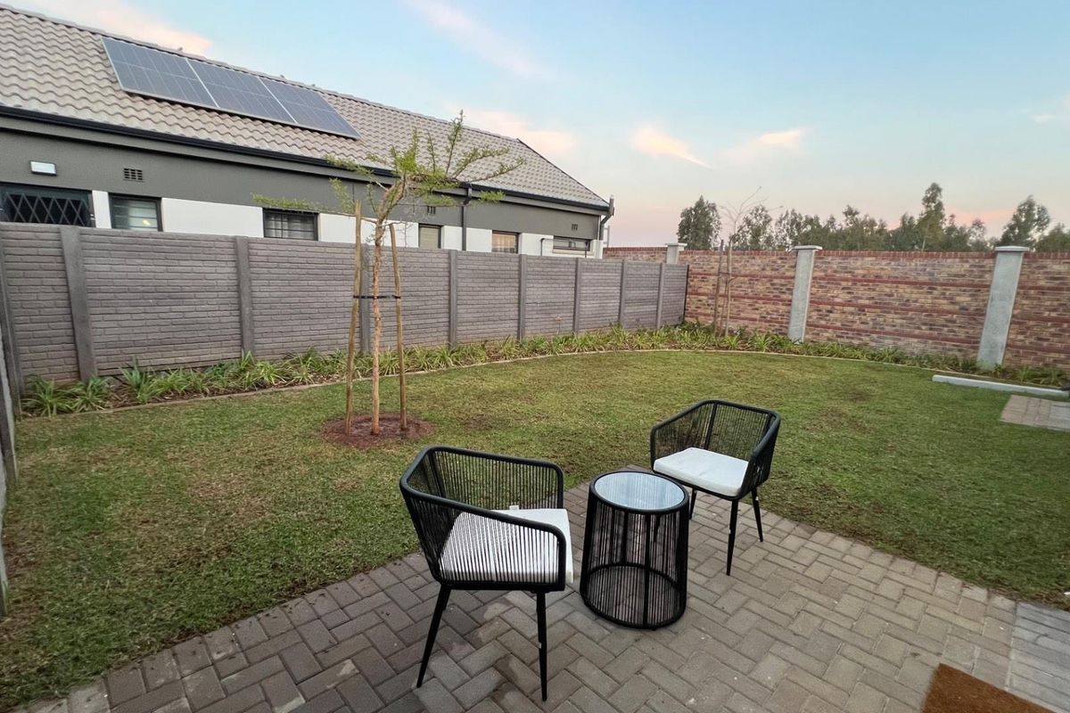 A private rear garden featuring a paved patio area, a well-maintained lawn, and perimeter boundary walls.