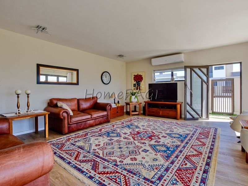 Spacious living room featuring laminate flooring, a wall-mounted split-system air conditioner, and direct access to an outdoor area through a security screen door.