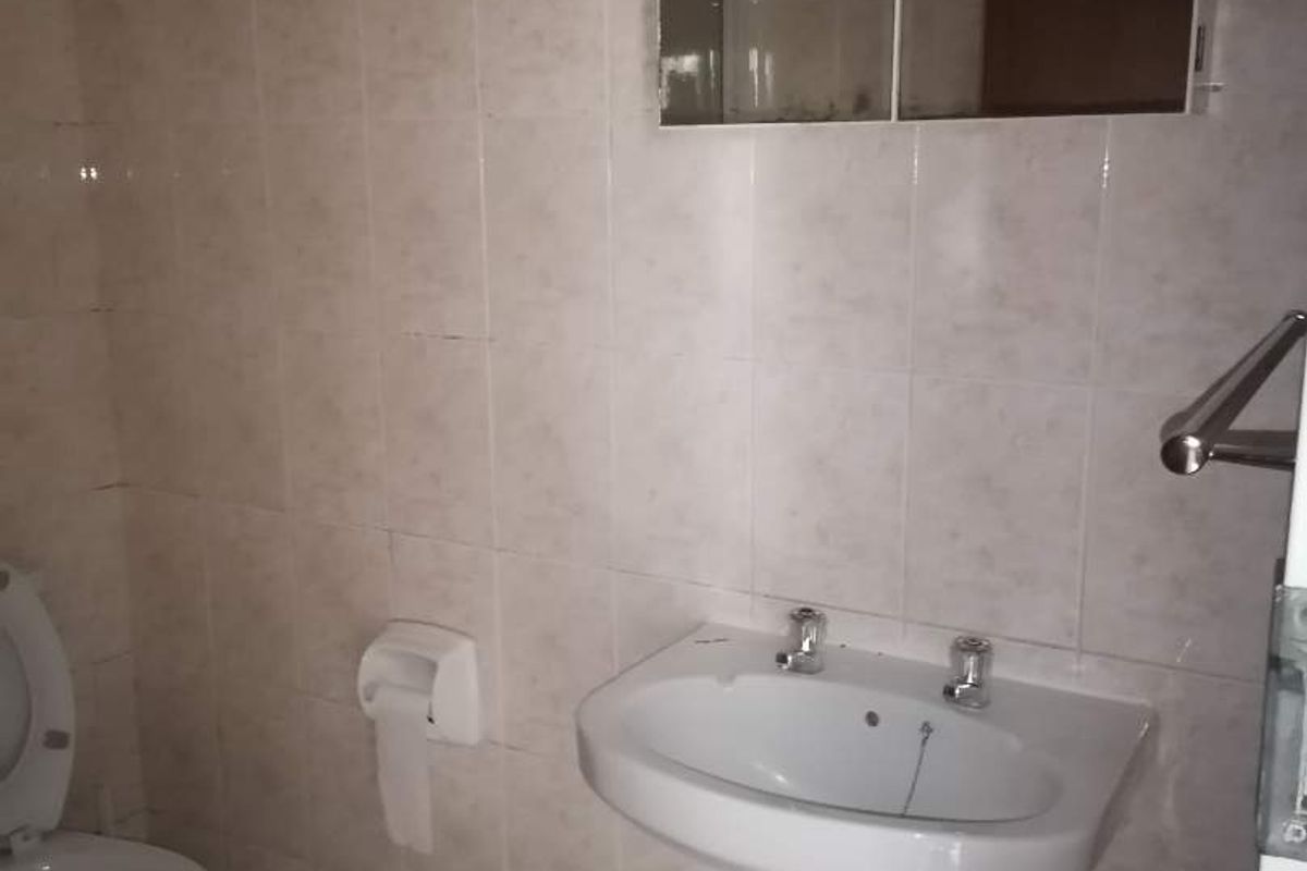 A functional bathroom featuring a pedestal sink, wall-mounted medicine cabinet, and a standard toilet with tiled walls and flooring.