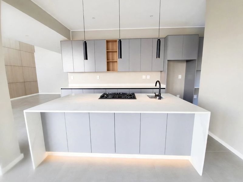 Modern open-plan kitchen featuring a central island with a gas hob, undermount sink, sleek grey cabinetry, and integrated under-cabinet lighting.