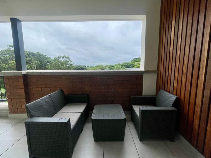 A covered balcony featuring tiled flooring, a brick balustrade, and decorative timber wall cladding, offering an open view of the surrounding landscape.