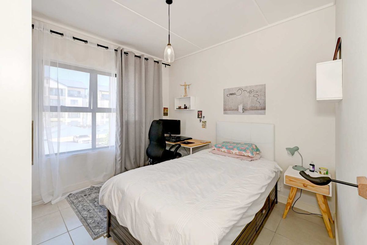 A bright and functional bedroom featuring neutral tiled flooring, a large window for natural light, and a modern pendant light fixture.