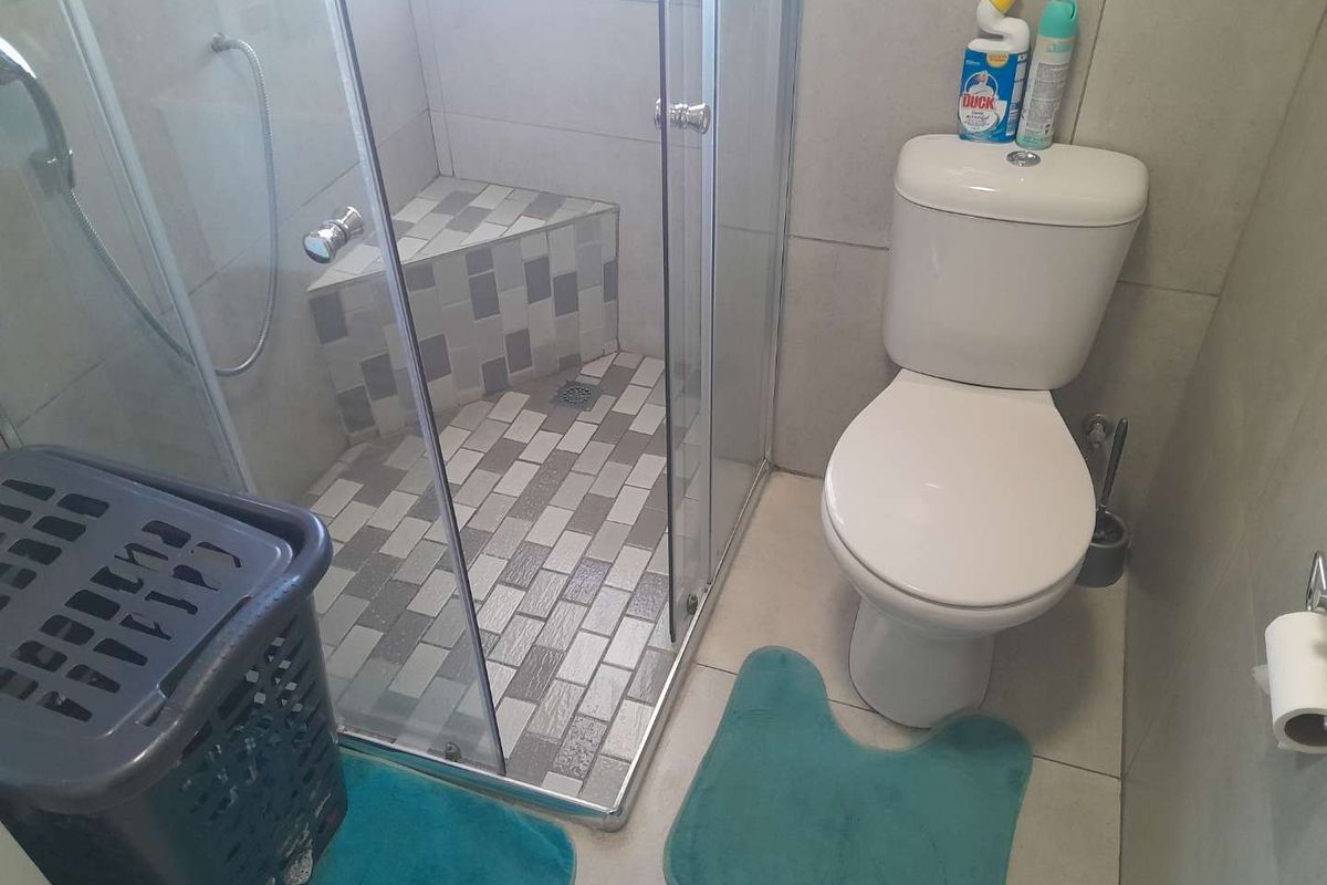 Compact bathroom featuring a glass-enclosed shower with built-in tiled seating and a standard white ceramic toilet.