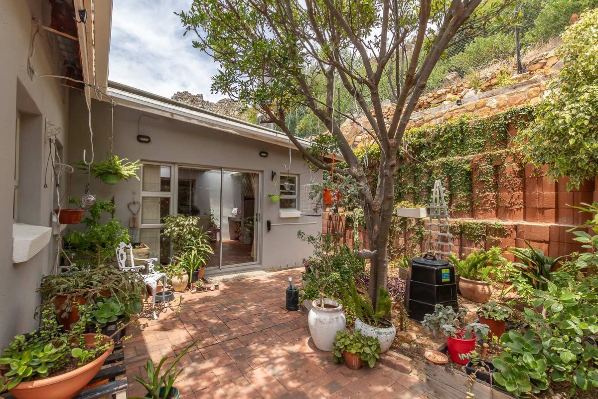 A private rear courtyard featuring brick paving, established trees, and a terraced retaining wall, providing a quiet outdoor space accessible from the main living area.