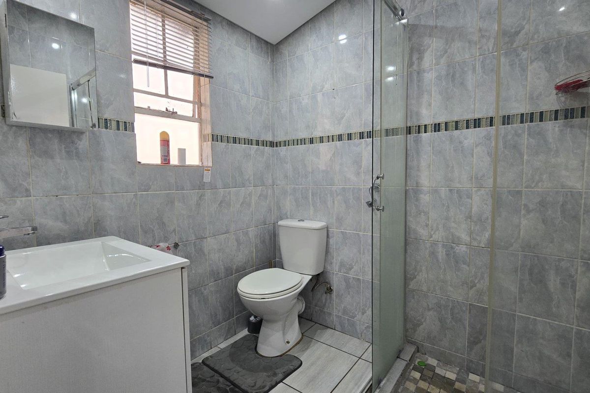 A functional bathroom featuring a vanity with basin, a toilet, and a glass-enclosed shower with grey tiled finishes throughout.