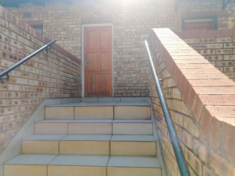 Exterior view of an apartment entrance featuring a face brick facade, tiled staircase, and metal handrails leading to a timber front door.