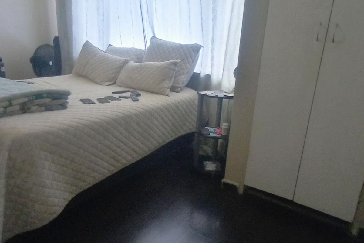 A bedroom featuring dark laminate flooring and a built-in white wardrobe.