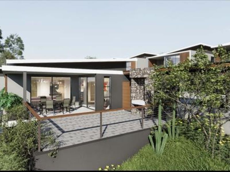 A modern rear exterior view featuring a paved patio, stone-clad chimney, and expansive sliding glass doors, showcasing contemporary architectural design.