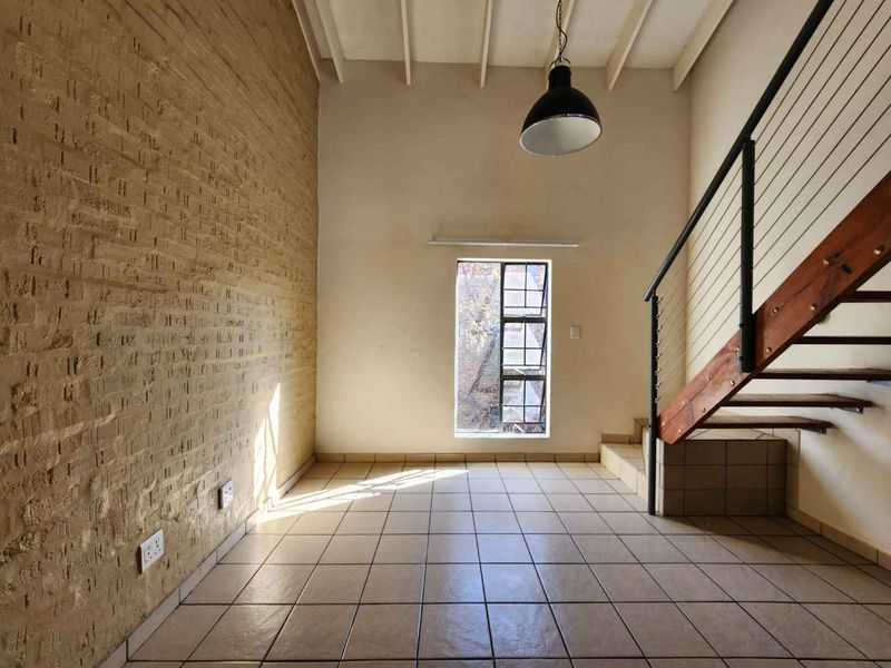 An empty living area featuring an exposed brick wall, tiled flooring, and a staircase with a metal railing, offering a unique industrial aesthetic.