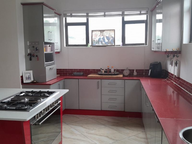 Modern kitchen featuring a central island with gas hob, ample built-in cabinetry, striking red countertops, and a tiled backsplash.