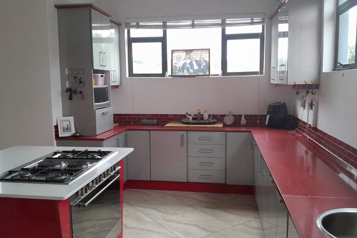 Modern kitchen featuring a central island with gas hob, ample built-in cabinetry, striking red countertops, and a tiled backsplash.