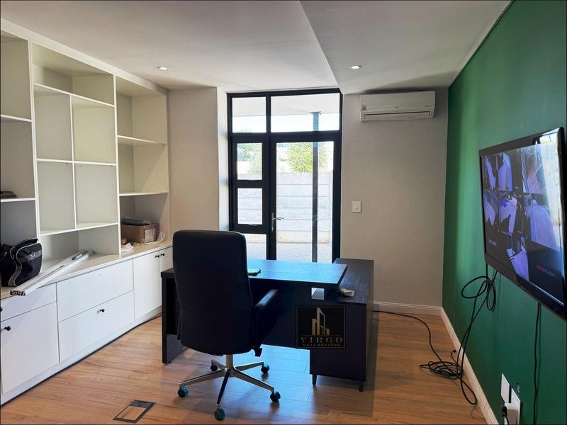 A functional home office featuring built-in white cabinetry, laminate flooring, a split-system air conditioner, and direct access to an outdoor area.