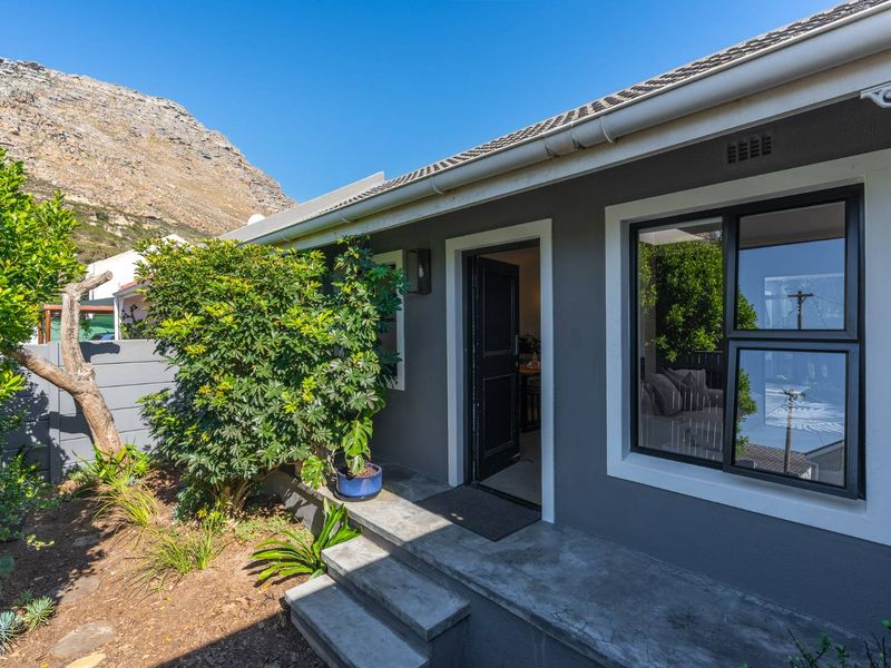 A well-maintained rear exterior view featuring concrete steps leading to an entrance, modern aluminium window frames, and a tidy garden area.