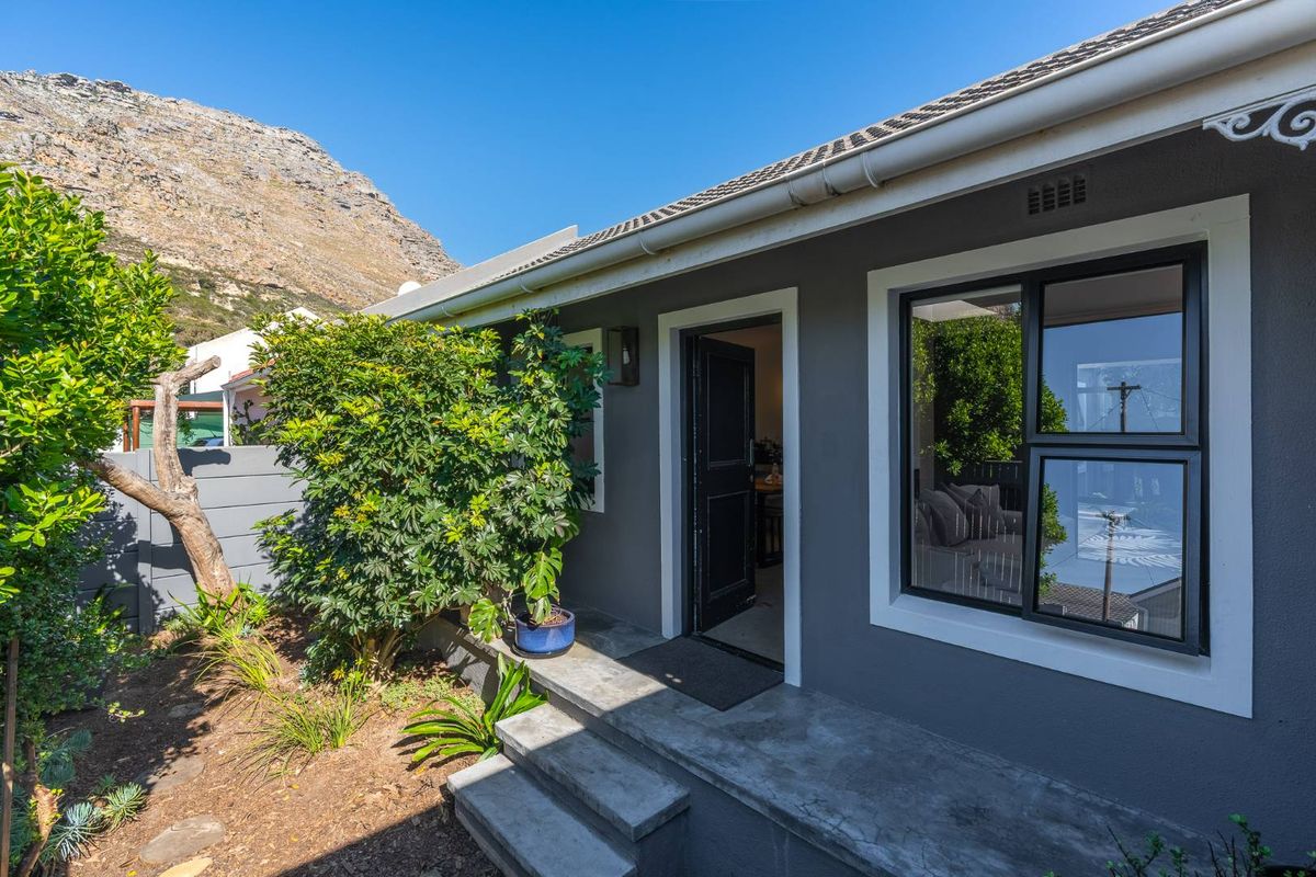 A well-maintained rear exterior view featuring concrete steps leading to an entrance, modern aluminium window frames, and a tidy garden area.