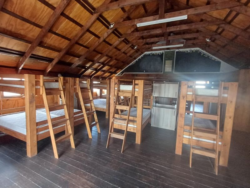 Spacious dormitory-style bedroom featuring exposed timber roof trusses, wood paneling, and dark timber flooring, providing a rustic accommodation setting.