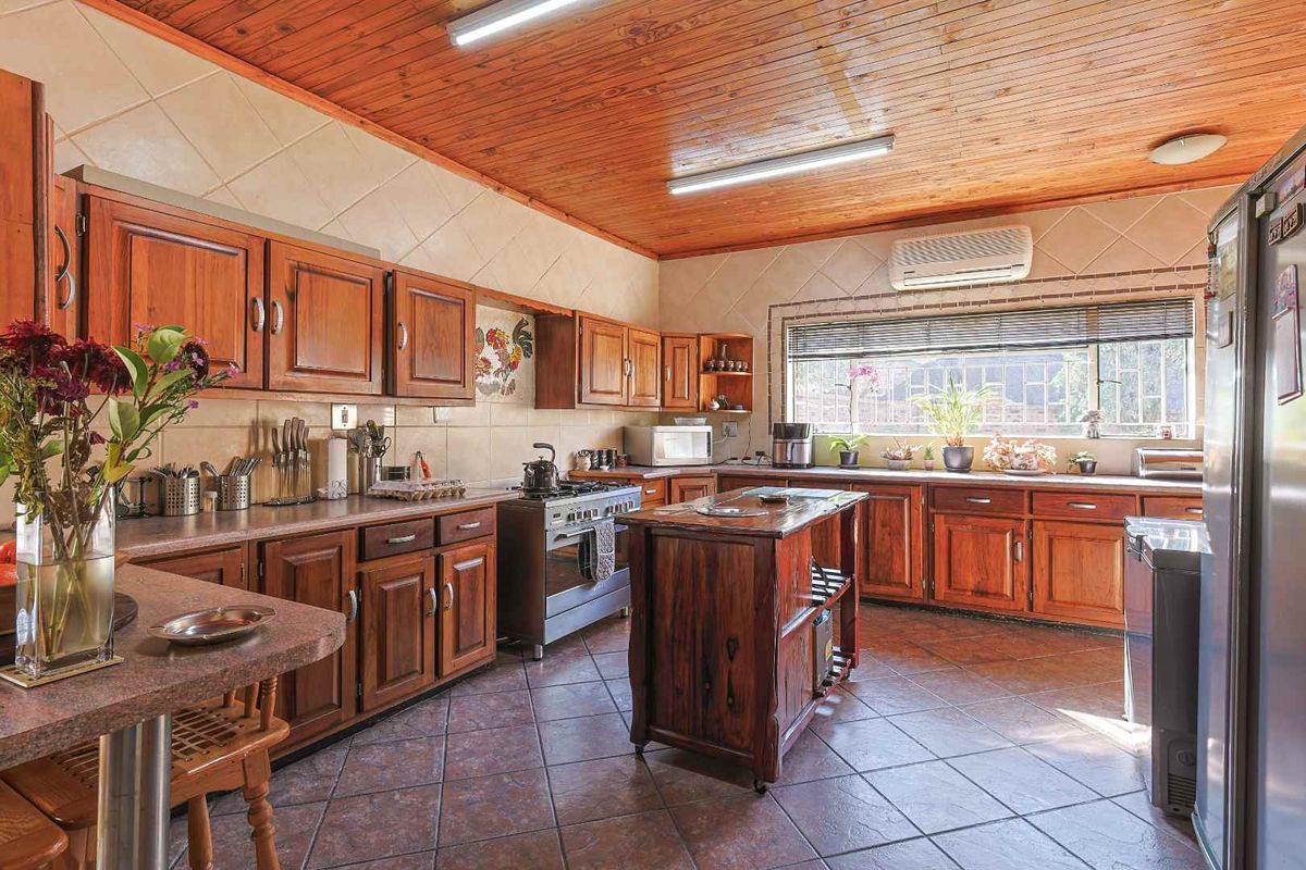 Spacious kitchen featuring wooden cabinetry, tiled countertops, a central island, and a distinctive timber-clad ceiling.