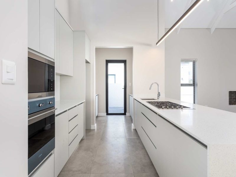 Modern, minimalist kitchen featuring a central island with gas cooktop, stone countertops, integrated appliances, and sleek cabinetry in a bright, open-plan layout.