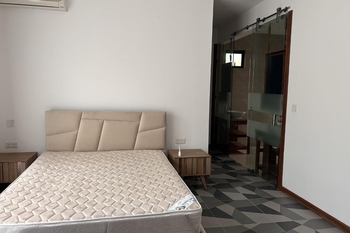 A modern bedroom featuring patterned floor tiles, a wall-mounted air conditioning unit, and a glass sliding door leading to an en-suite bathroom.