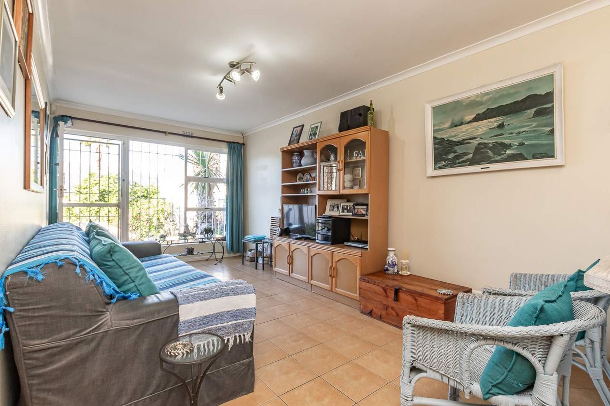 A comfortable living room featuring tiled flooring, cove cornicing, and a large sliding glass door with security bars providing natural light.
