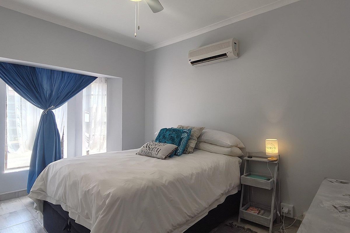 A well-lit bedroom featuring tiled flooring, a ceiling fan, and a wall-mounted air conditioning unit.