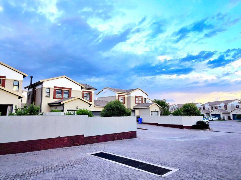 A wide-angle view of a townhouse complex featuring paved driveways, boundary walls, and multiple residential units under a dramatic sky.