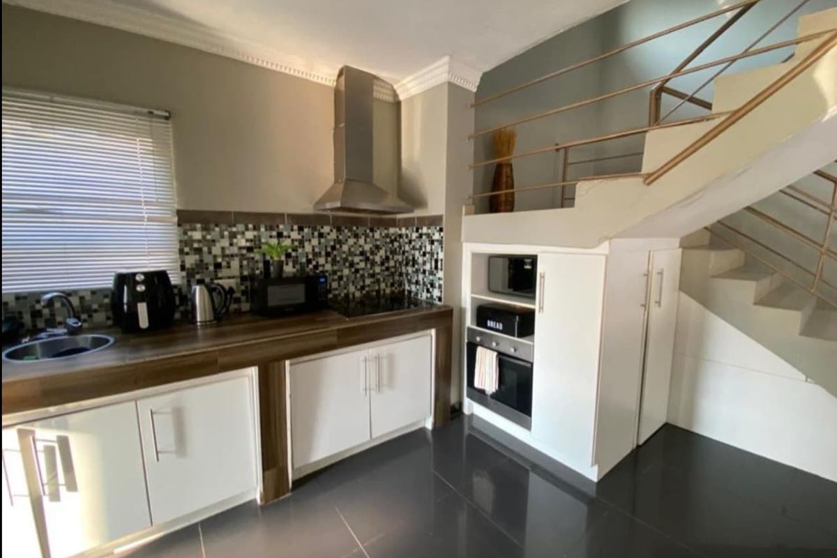 Modern kitchen featuring white cabinetry, wood-look countertops, mosaic tile backsplash, stainless steel extractor fan, and built-in oven, situated beneath a staircase.