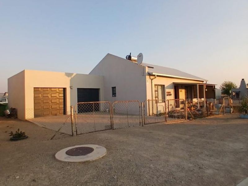 Front view of a single-story house featuring a double garage, solar water heater, and a covered patio area with chain link perimeter fencing.