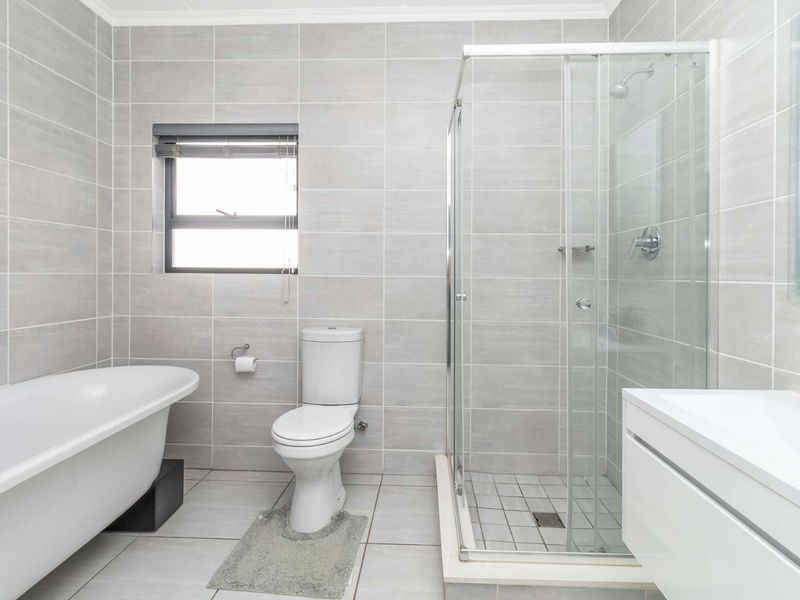 Modern bathroom featuring a freestanding bathtub, separate glass shower enclosure, toilet, and a sleek vanity cabinet with neutral grey wall and floor tiling.
