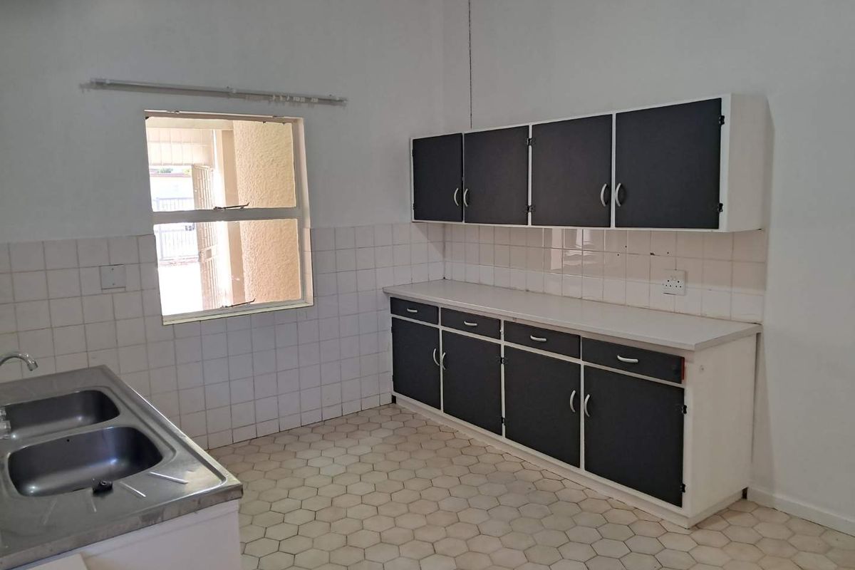 A functional kitchen featuring built-in cabinetry, a double stainless steel sink, and tiled splashbacks, offering a blank canvas for potential renovation.
