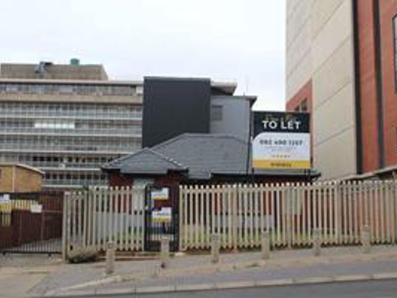 Front exterior view of the property featuring security fencing and gated access, situated in an urban environment with a prominent to-let sign.