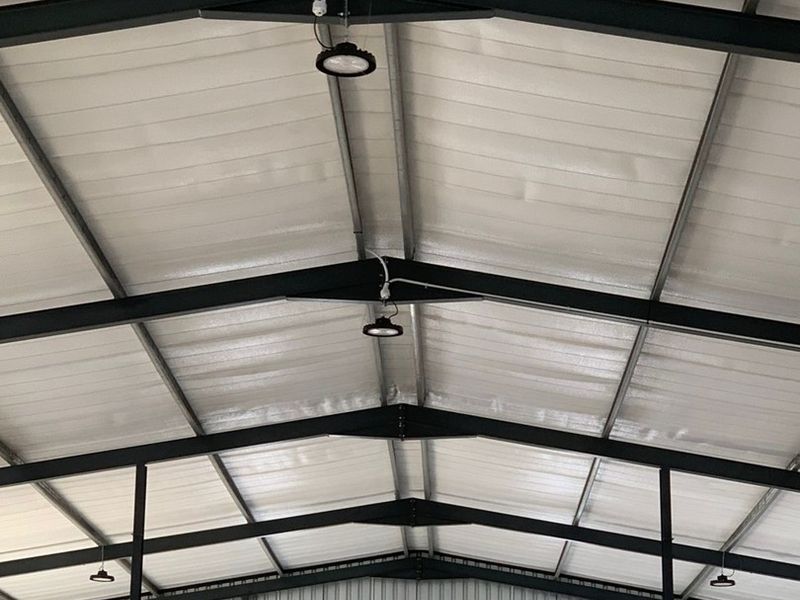 Interior view of an industrial warehouse space featuring a high-clearance steel portal frame structure with corrugated metal roofing and integrated industrial lighting.