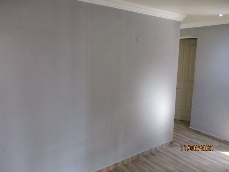 A clean, empty hallway featuring neutral grey walls, coving, and modern wood-look tiled flooring leading to an internal doorway.