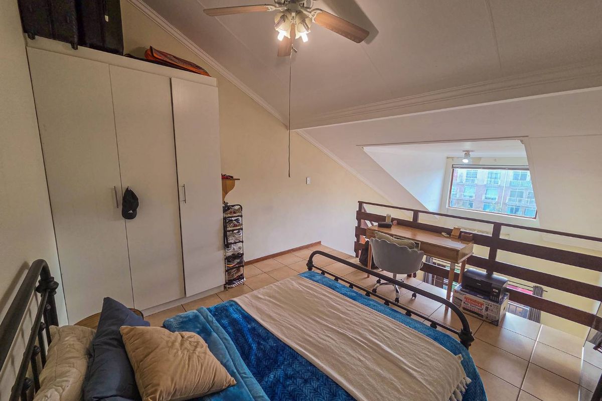 Loft-style bedroom featuring a vaulted ceiling, built-in wardrobe, tiled flooring, and a mezzanine overlook with a wooden balustrade.