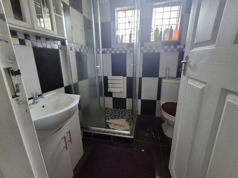 A compact bathroom featuring a shower enclosure, vanity basin, and toilet with a distinctive black and white checkered tile design.