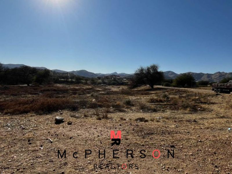 A wide-angle view of an undeveloped commercial land plot featuring natural terrain and distant mountain scenery.