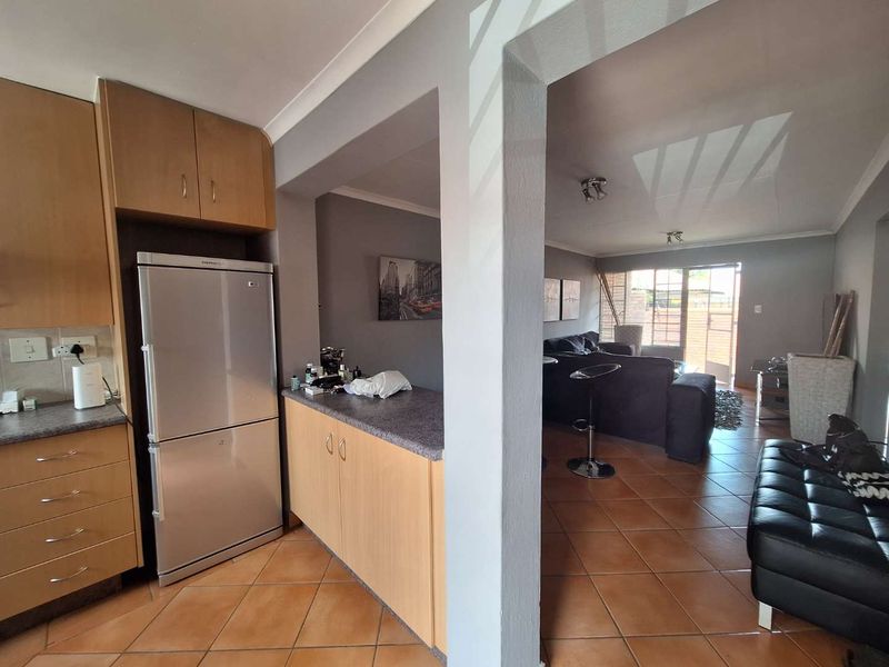 Open plan kitchen and living area featuring tiled flooring, wooden cabinetry, and direct access to an outdoor patio through a sliding glass door.