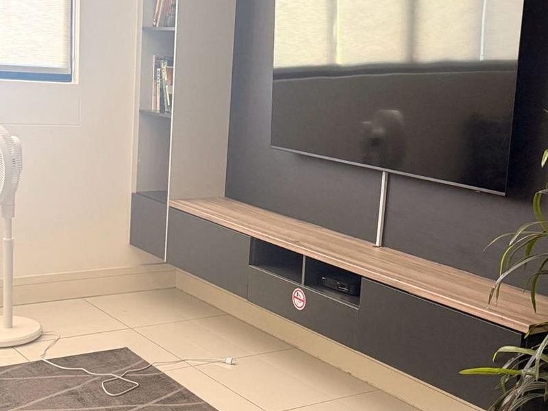 A modern living room featuring a sleek, dark-toned floating media console with integrated shelving and neutral tiled flooring.