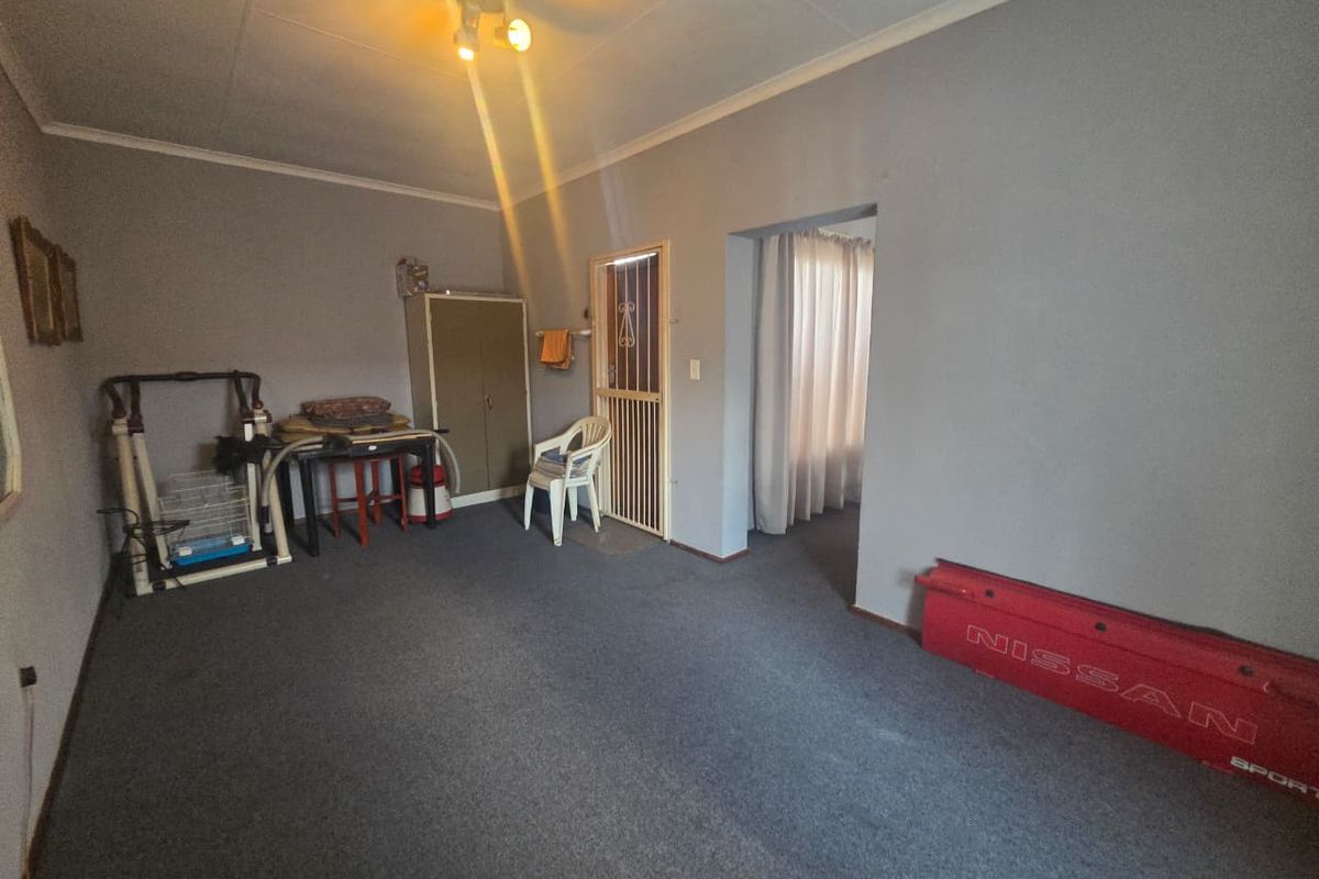 A spacious living area featuring grey carpeting, neutral wall tones, and a security gate leading to an adjacent room.