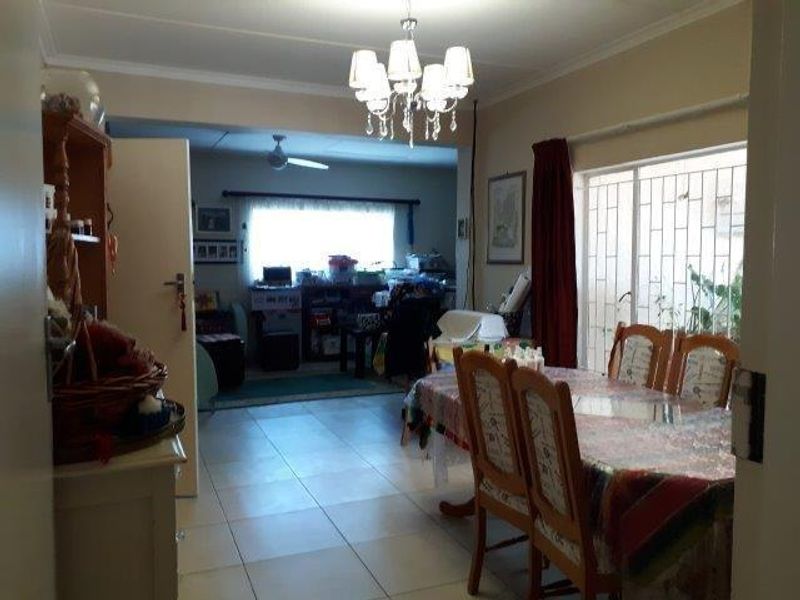 Open plan living and dining area featuring tiled flooring, a ceiling fan, and decorative chandelier lighting with security bars on the windows.